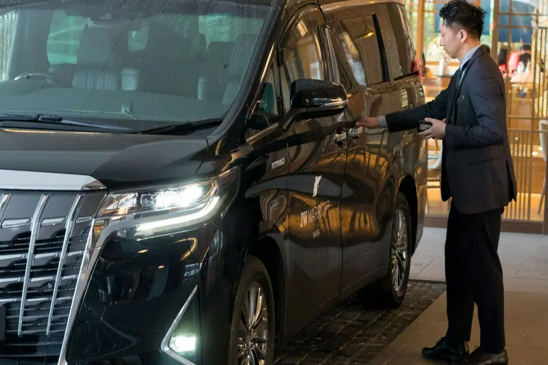 Chauffeur in a suit beside a black people carrier, ready for a private transfer